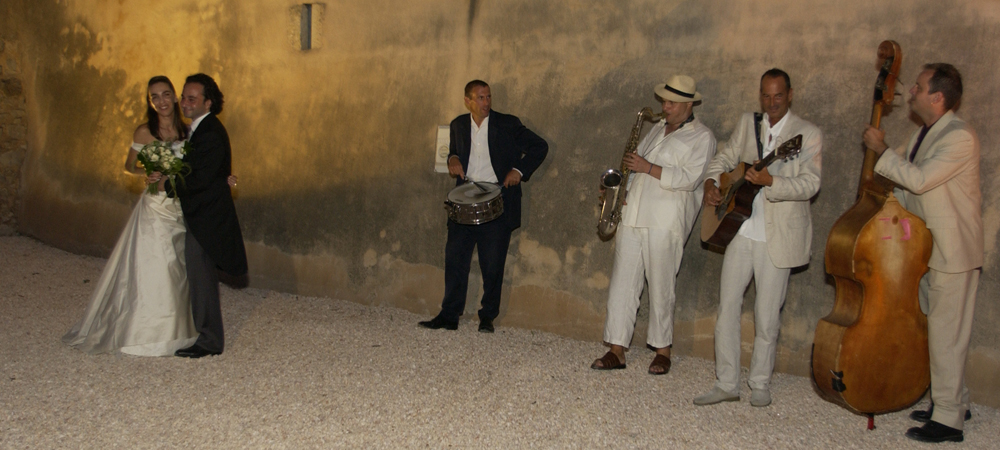 Moment festif de jeunes mariés accompagnés d’un groupe de musiciens en tenue élégante lors d’une réception de mariage en extérieur
